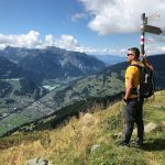 man standing beside signboards on pole on grass mountain during day