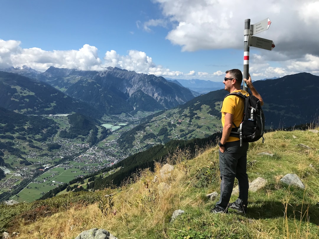 man standing beside signboards on pole on grass mountain during day