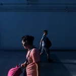 woman walking near man beside white wall at daytime