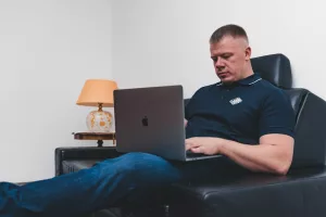 man in black polo shirt sitting on black leather couch using macbook